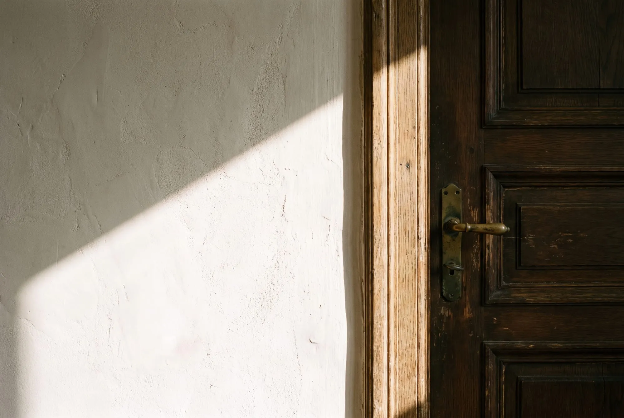 Daylight across a whitewashed wall and a wooden door handle